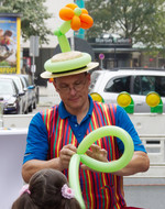 Carsten Rogmann von der Firma Kiro Kinderunterhaltung bastelt eine Ballonfigur. Ein kleines Mädchen schaut zu. 