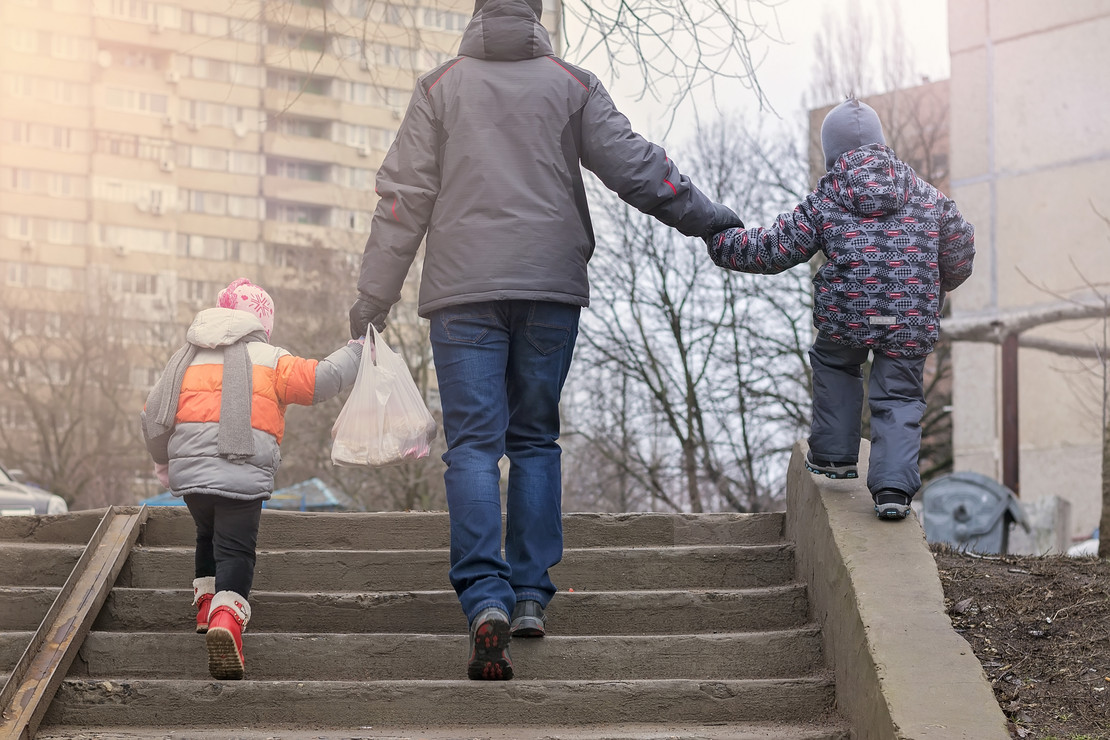 Elternteil mit zwei kleinen Kindern in einem Plattenbauviertel