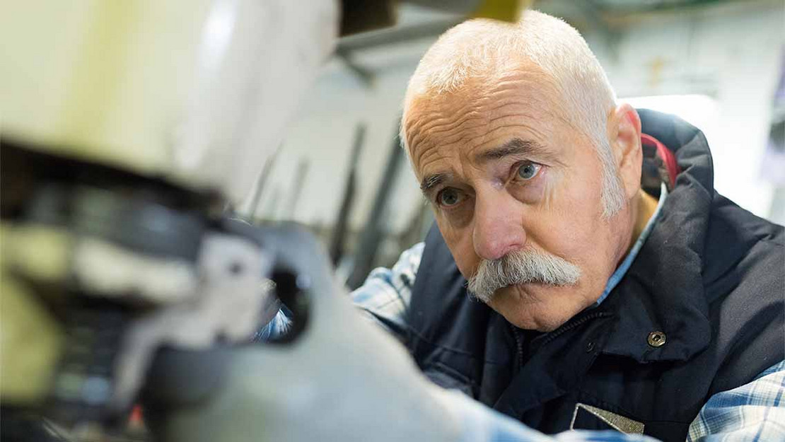 Älterer Mann arbeitet in einer Fabrik an einer Maschine. 