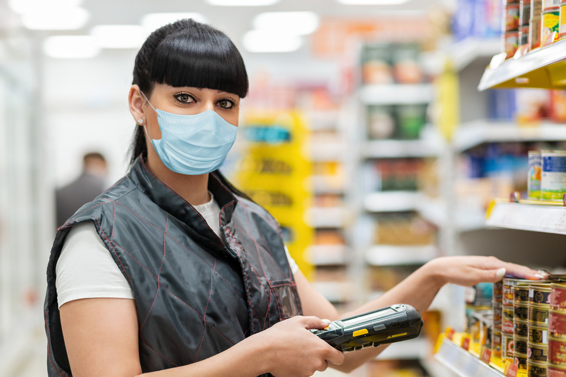 Beschäftigte im Supermarkt arbeitet mit Maske am Regal. 