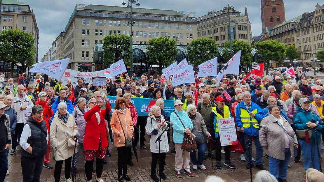 Gruppe von Menschen mit SoVD-Flaggen steht auf einem Platz in Hamburg. 