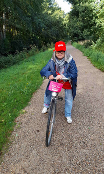 Eine Radfahrerin steht mit ihrem Rad auf einer Straße, die am Wald lang führt