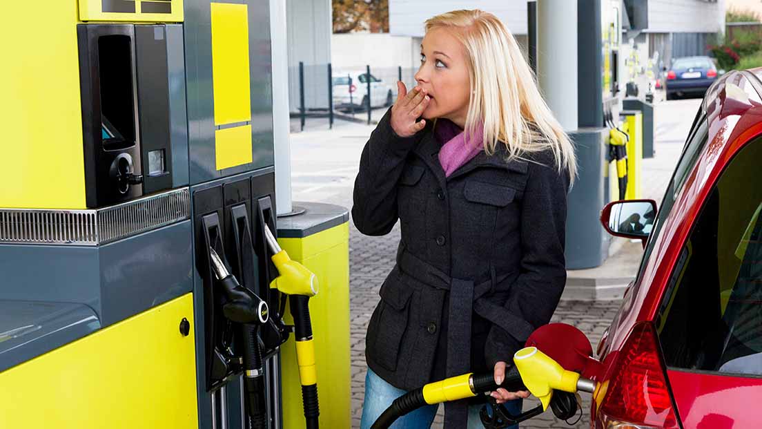 Eine Frau tankt ihr Auto auf und blickt erstaunt auf die Preisanzeige.